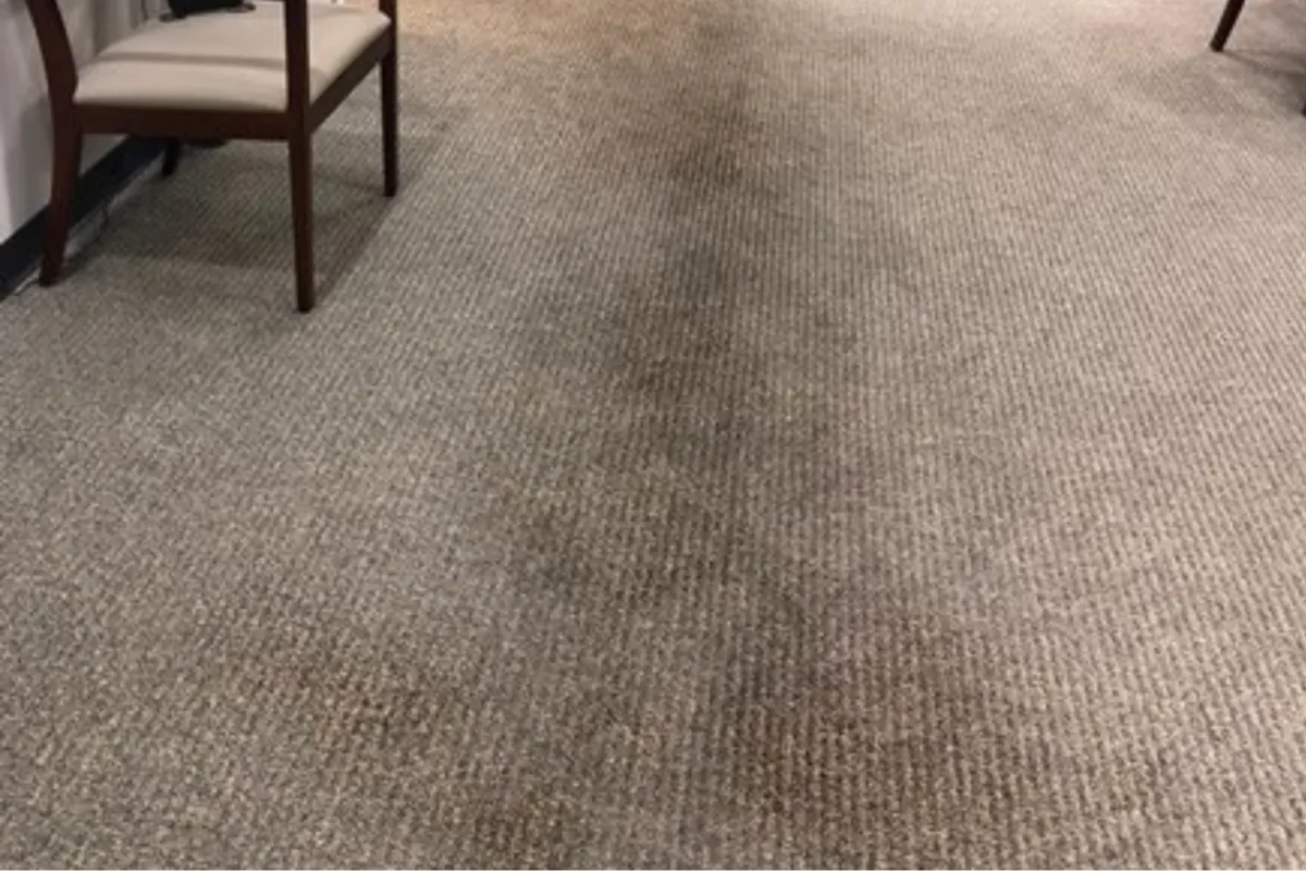 Beige loop-pile commercial office carpet with large V-shaped dark stain across the center before cleaning in NYC