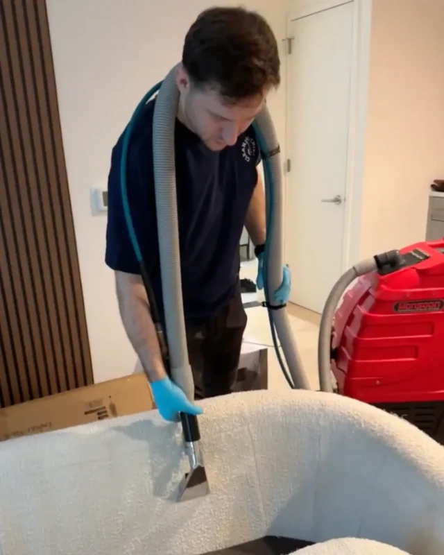 Cleaning Chief cleaner using upholstery steam wand on white boucle armchair in NYC apartment