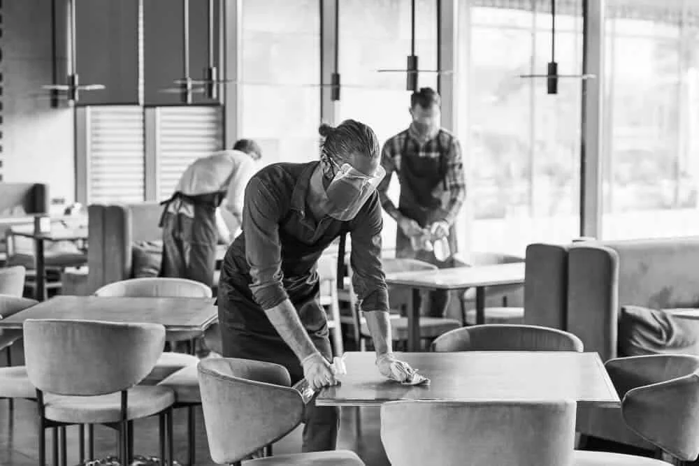 Professional cleaning crew in protective gear sanitizing restaurant tables in a New York City commercial space