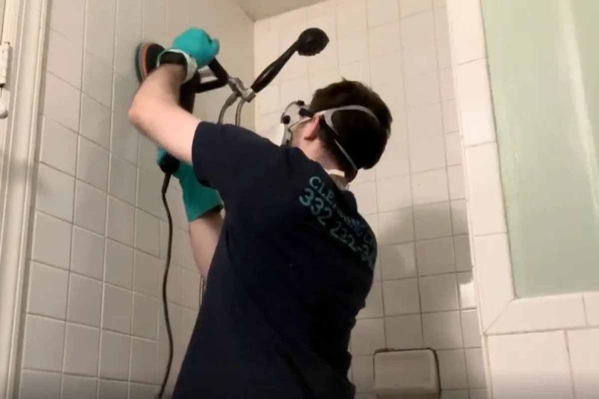 Cleaning Chief technician with safety glasses operating a rotary scrubbing machine on white bathroom tile and grout