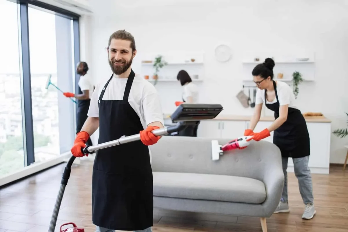 Team of four Cleaning Chief NYC technicians in black aprons with red gloves cleaning a modern NYC apartment living room — vacuuming floors and steam cleaning furniture