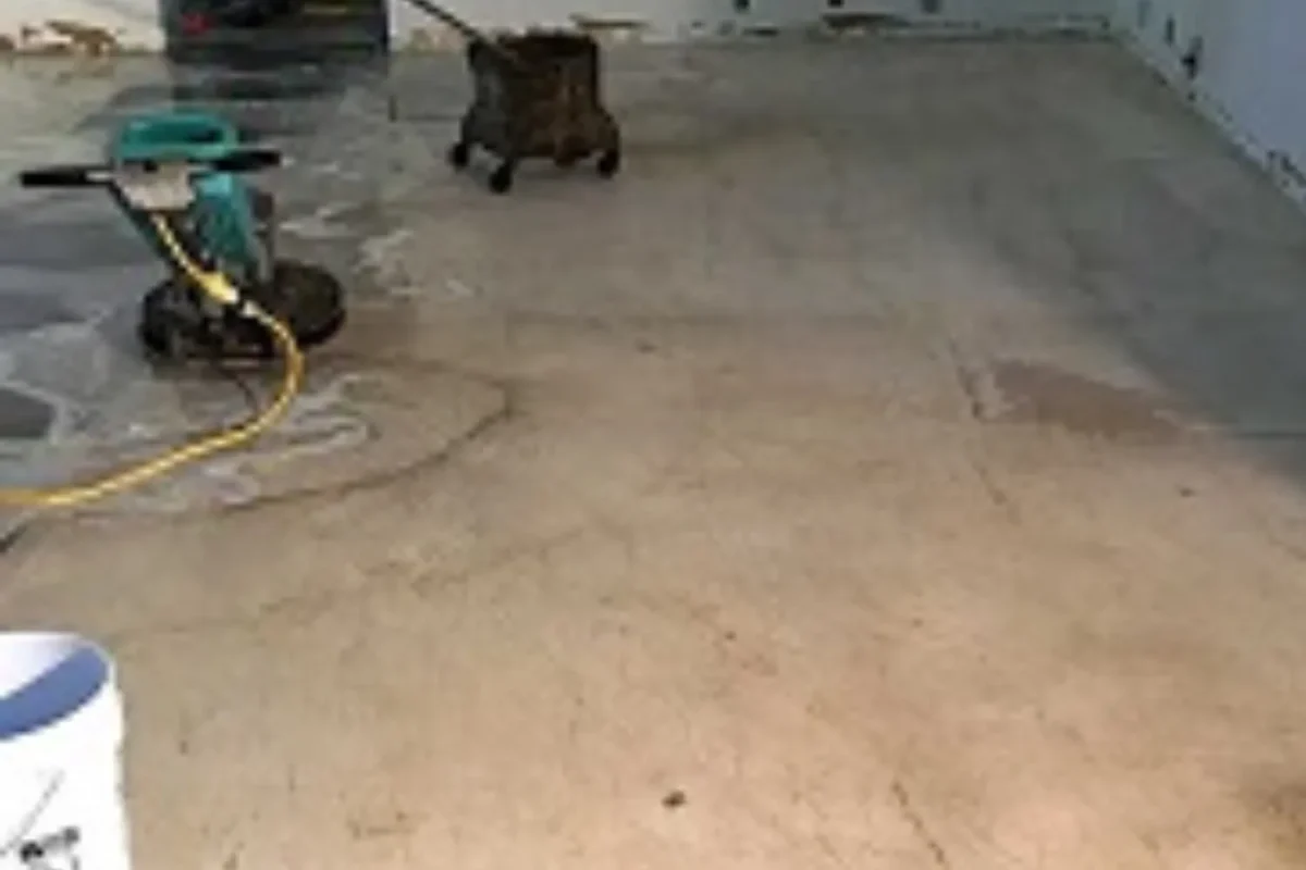Large commercial warehouse floor being scrubbed with floor scrubber machine showing wet cleaned surface during service