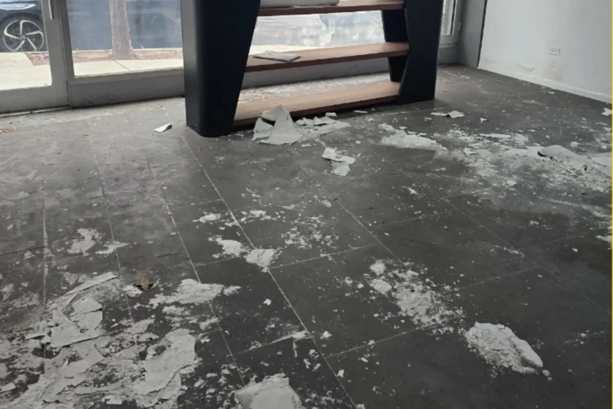 Dark tile floor covered in construction debris and plaster chunks scattered across commercial space before deep cleaning