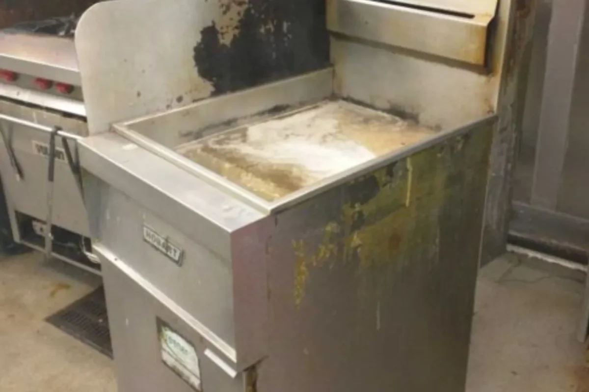 Commercial kitchen deep fryer basin heavily caked with black grease and thick carbon buildup before deep cleaning