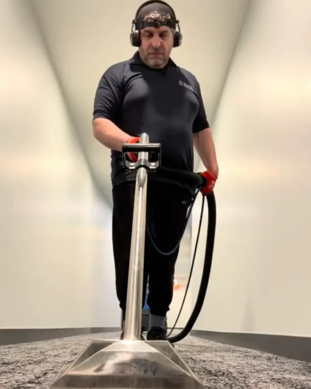 Cleaner with headphones using hot water extraction wand on dark charcoal commercial carpet during deep cleaning in NYC
