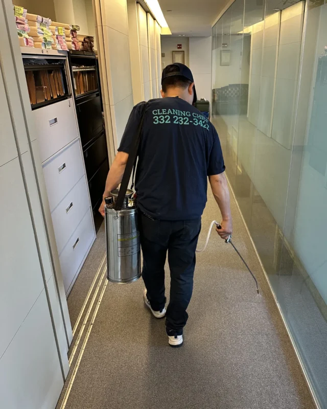 Cleaning Chief technician carrying stainless spray canister through glass-walled NYC office corridor for commercial deep clean