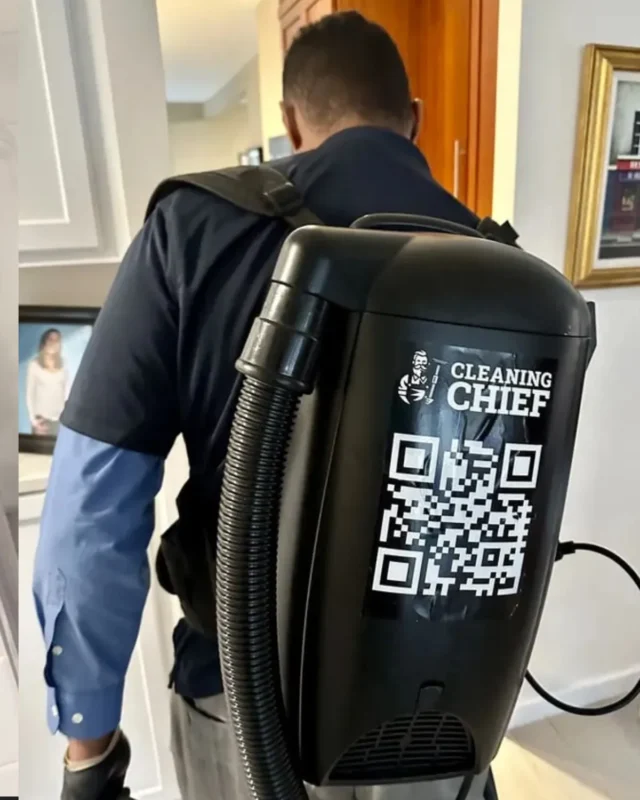 Cleaning Chief cleaner with branded backpack vacuum in NYC apartment hallway
