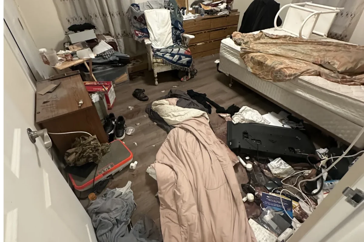 Severely cluttered NYC bedroom with clothes and debris covering the floor before deep cleaning