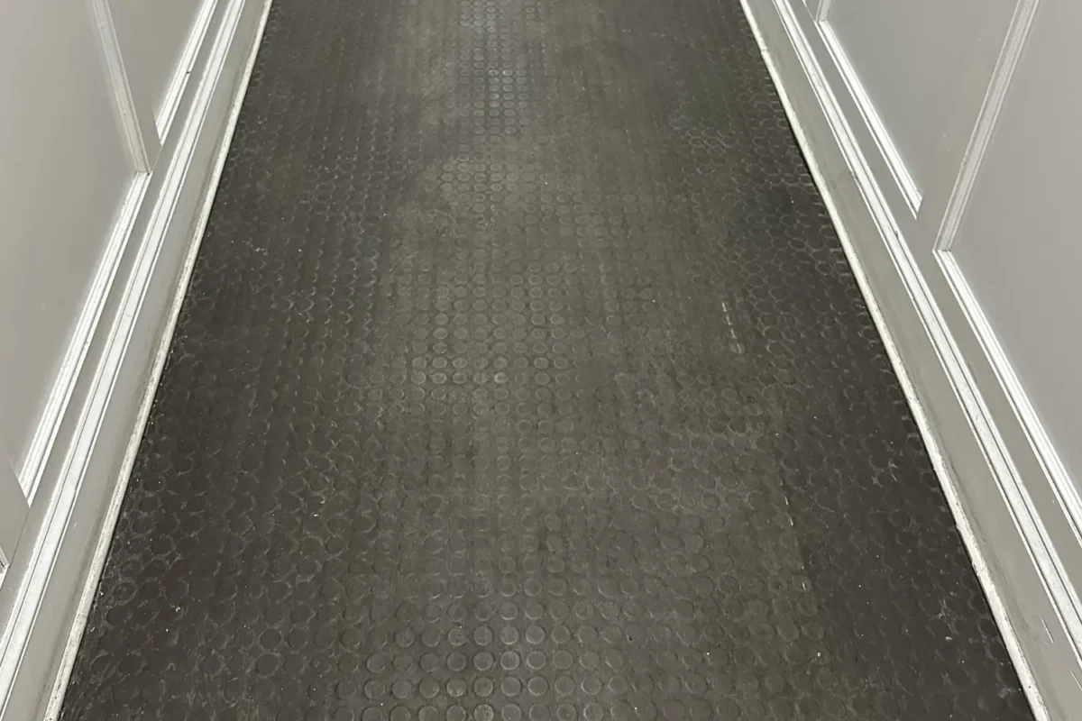 Dull and grimy rubber coin-dot floor in NYC apartment hallway before floor buffing service