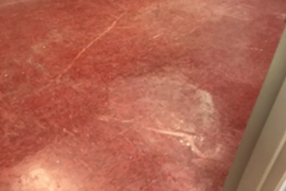 Close-up of dull scratched red or rose-colored stone floor surface with hazy matte finish before floor care treatment