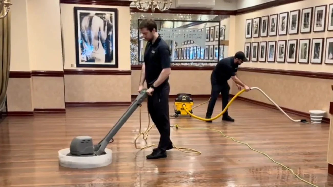 Two Cleaning Chief technicians buffing and extracting hardwood floor in NYC commercial hall with wall art and chandelier