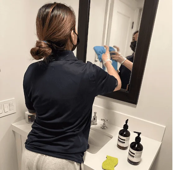 Cleaning Chief NYC maid cleaning and polishing a bathroom mirror to a streak-free finish