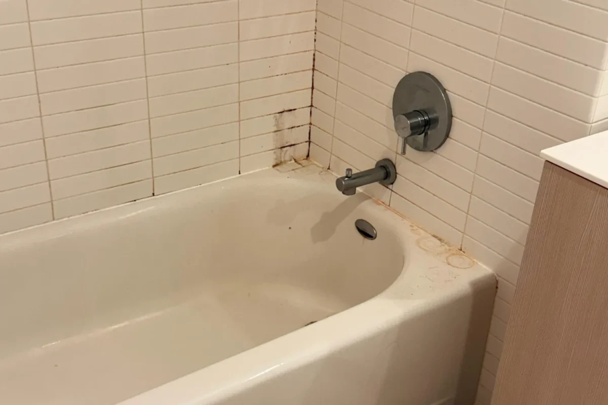 Bathtub with black mold on grout and yellowing stains around drain before move-out cleaning in NYC