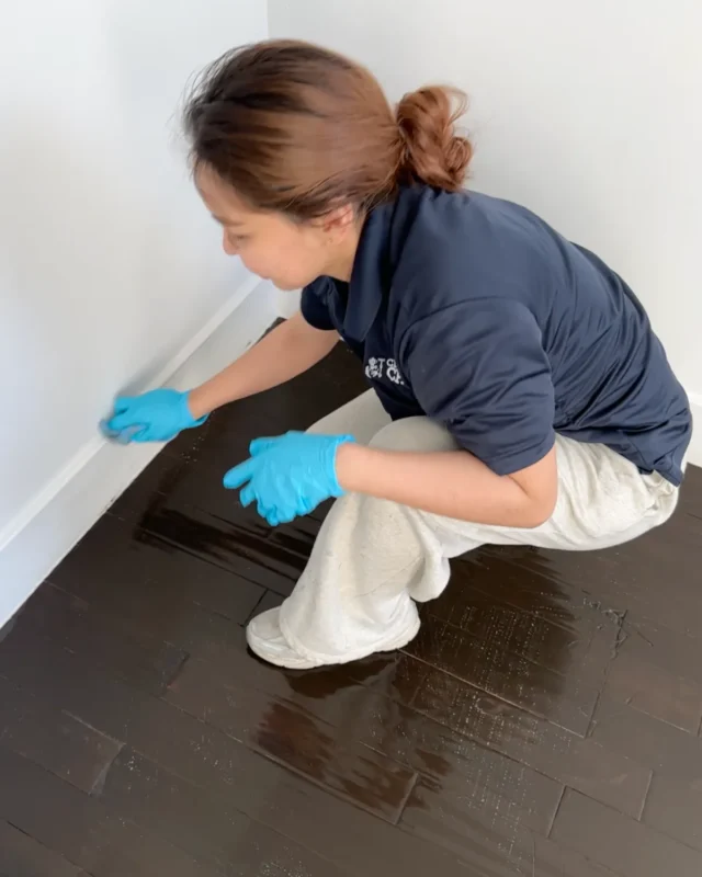 Cleaning Chief cleaner scrubbing dark hardwood floor and baseboards by hand during move-out cleaning