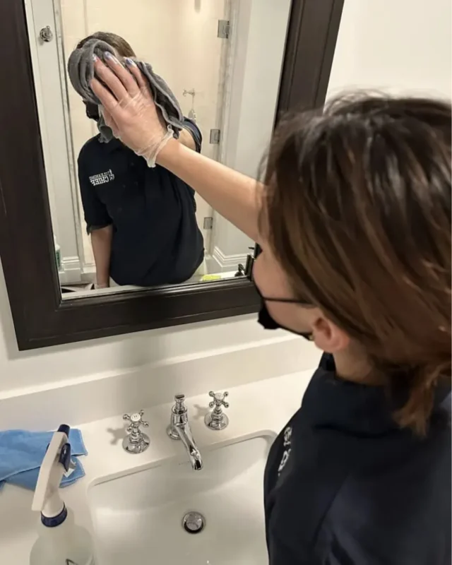 Cleaning Chief cleaner wiping bathroom mirror with microfiber cloth during move-out cleaning in NYC