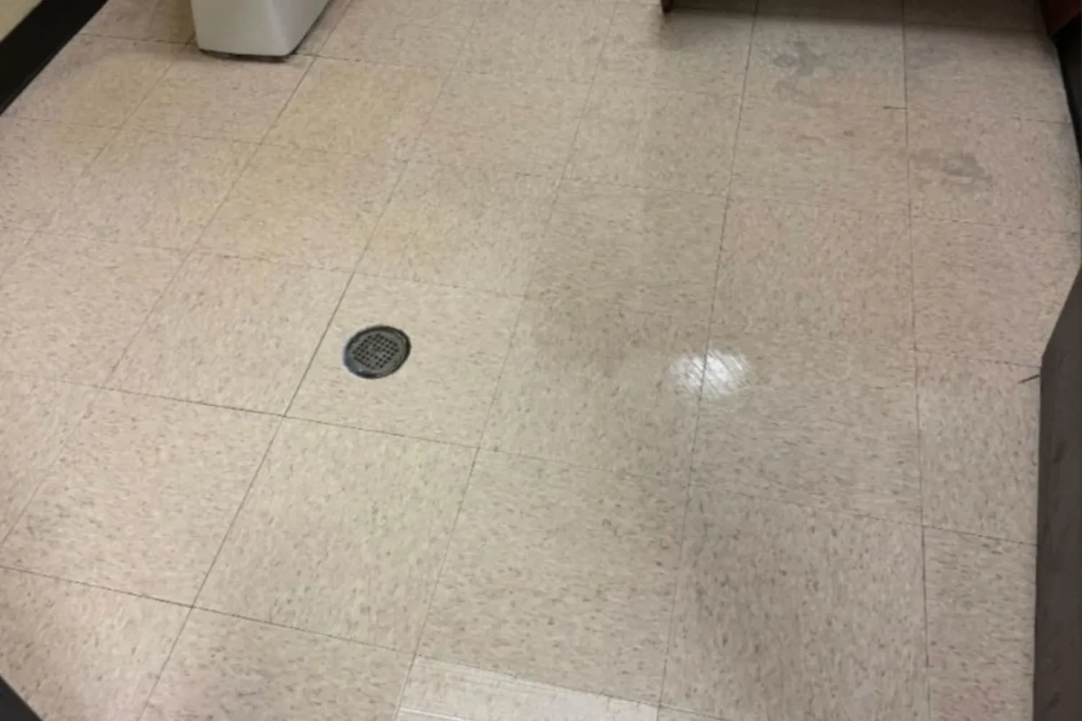 Same commercial restroom floor now clean and partially reflective with clear drain after professional office cleaning