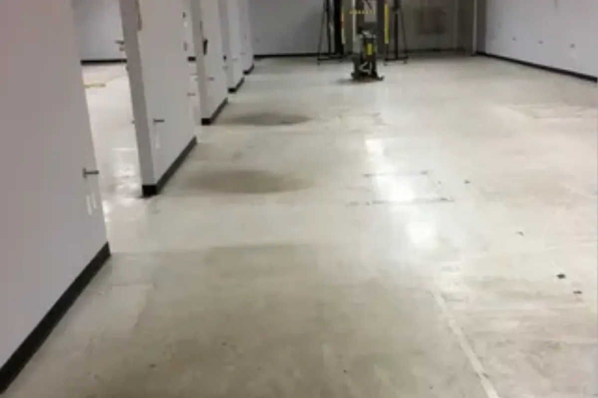 Large commercial warehouse or office space with dull dirty concrete floor and floor buffer machine in background