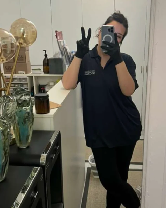 Cleaning Chief female cleaner in black polo giving peace sign in mirror selfie inside commercial office space