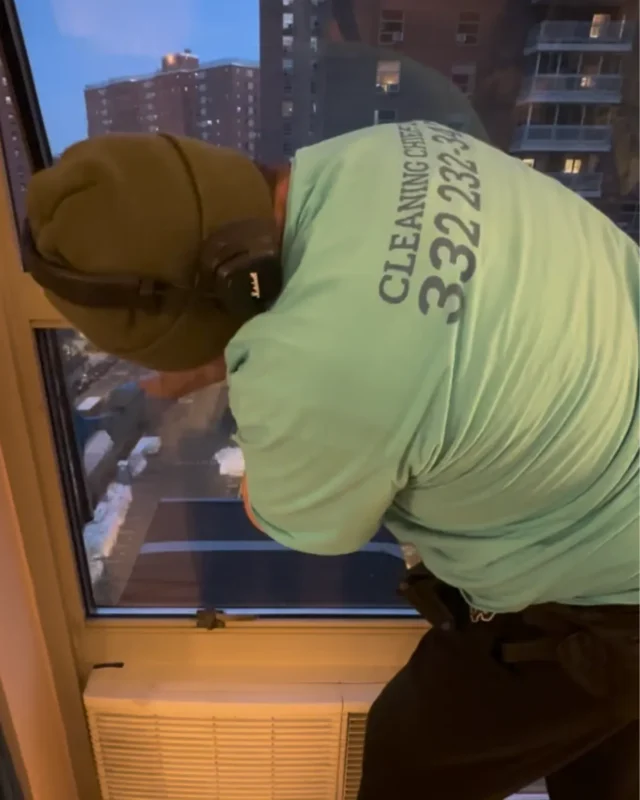Cleaning Chief cleaner scrubbing window frame with NYC skyline visible outside at night