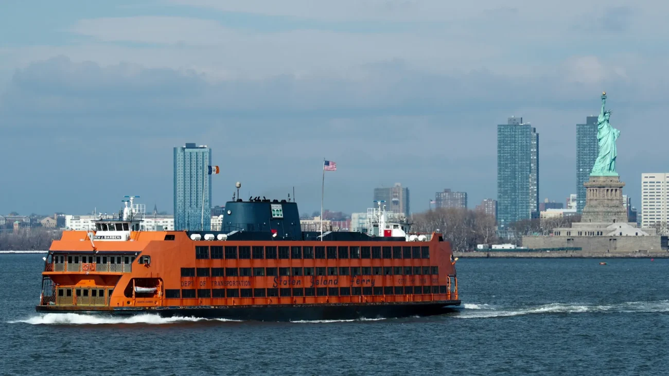 Orange Staten Island Ferry crossing New York Harbor with the Manhattan skyline and Statue of Liberty in the background