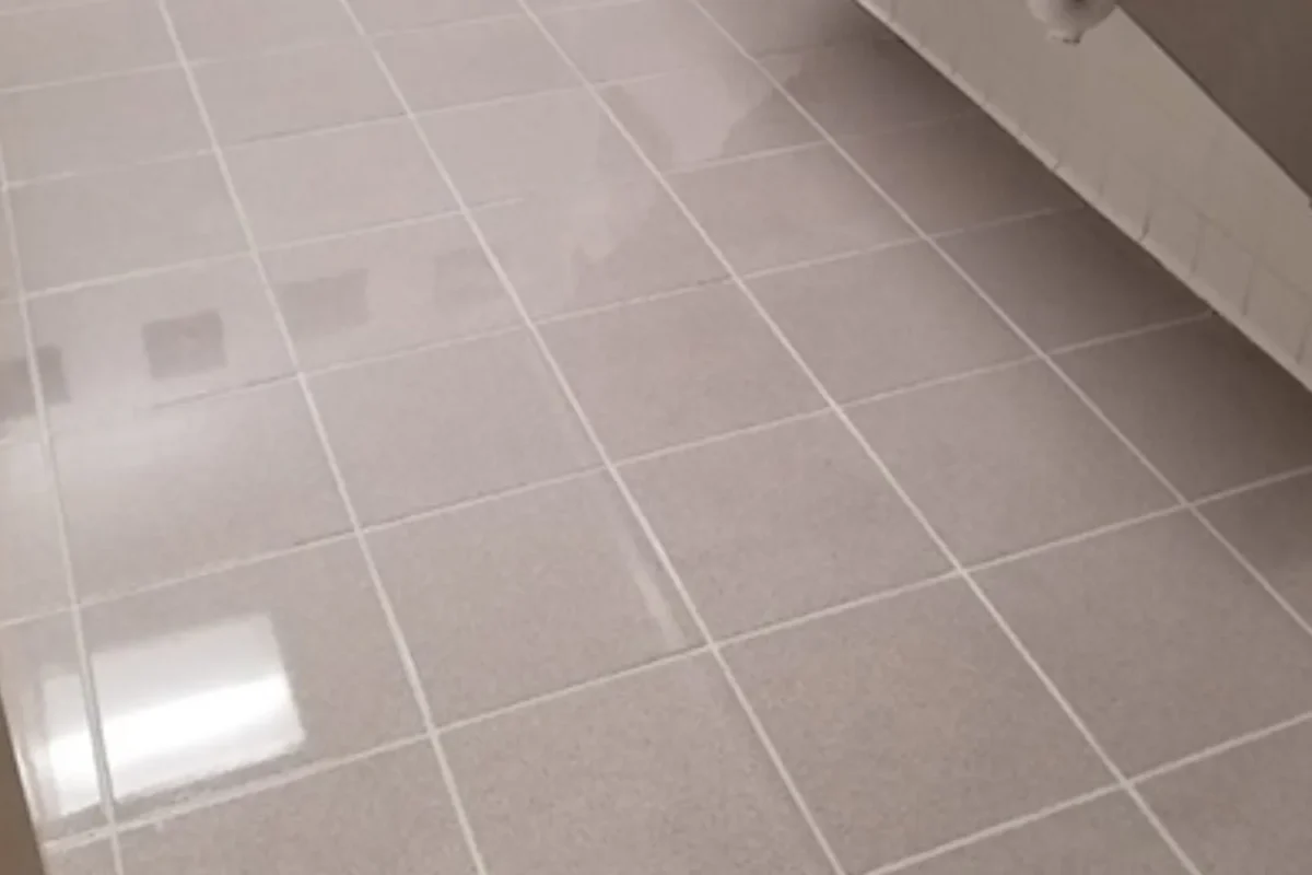 Same gray bathroom floor tiles now bright and reflective with clean grout after commercial power washing in NYC