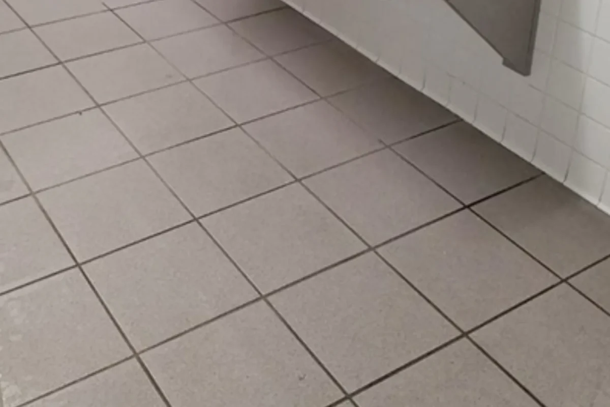Gray commercial bathroom floor tiles with heavily soiled grout and dirty surface before power washing in NYC
