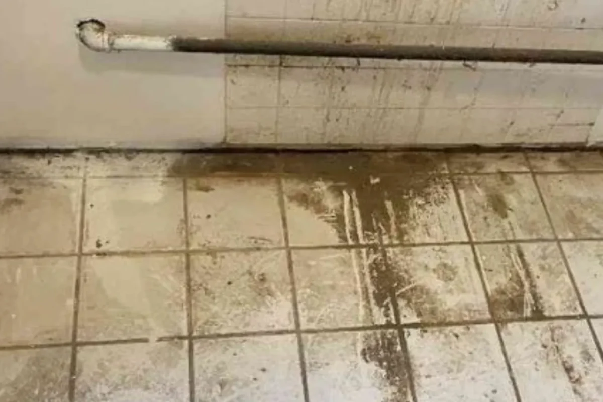Commercial tile floor and base of wall heavily coated in dried mud and caked grime before power washing in NYC