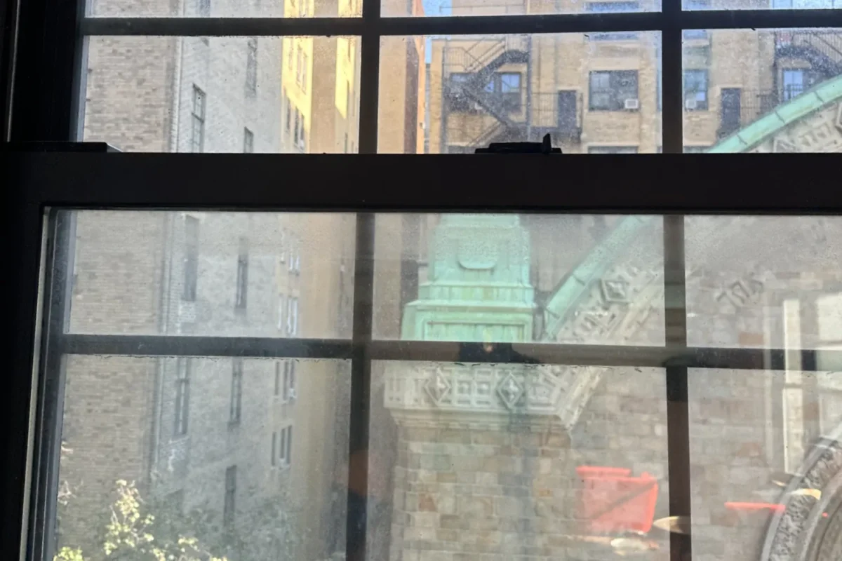 Multi-pane NYC apartment window hazy with accumulated dust and city grime before professional cleaning